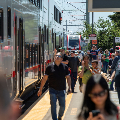 Large crowd outside new electric train on platform.